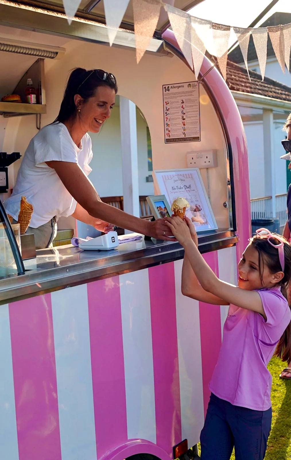 A Jersey Belle scoop being handed from the pink trailer window to a smiling girl